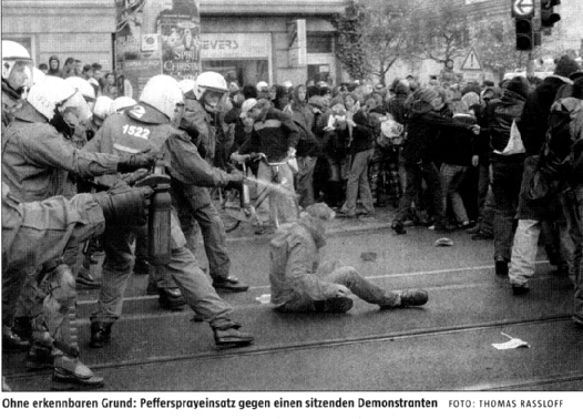 taz-nord vom 23.11.2006: Keule gegen NPD-Gegner. Das Foto zeigt Daniel, wie er nach einem durch einen Sturz verursachten Rippenbruch verletzt auf der Stra�e sitzt, w�hrend ihn Polizisten ihn von hinten mit Pfefferspray misshandeln.